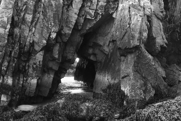 Black and white view of small tunnel in sea cliff caused by coastal erosion