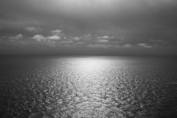 Black and white view of an empty ocean with sunlight reflecting on surface of calm water