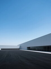 Modern minimalist building with a flat roof and large windows under a clear blue sky.