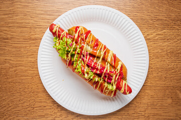 A delicious hot dog topped with lettuce, ketchup, and creamy sauce awaits on a plate