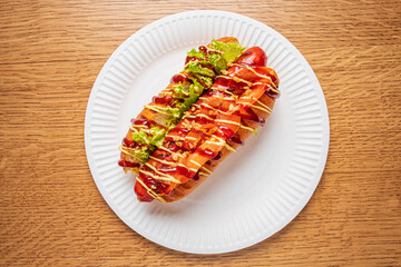 A beautifully crafted hot dog features a variety of colorful toppings and sauces on a white plate
