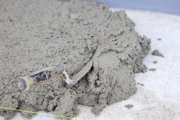 Construction scene featuring a gray concrete surface, a trowel, pull tabs, and wedges used for tile leveling, essential for precision and quality.