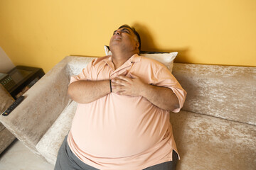Emergency - obese Indian man have heart attack at home. Overweight fat guy suffer chest pain. Healthcare and medical condition. Top angle.