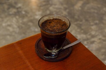 A rich, dark cup of Robusta coffee on a rustic wooden coaster, with a spoon beside it. Perfect for coffee shops, morning rituals, and cozy atmosphere themes.