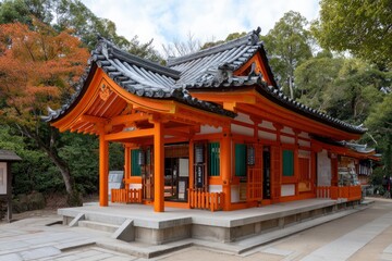 Naklejka premium An orange and white Japanese building with a gray tiled roof sits on a concrete platform surrounded by green trees