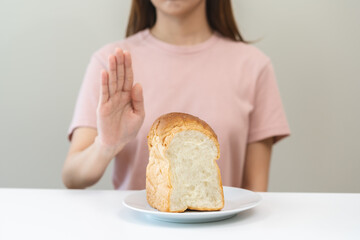 Gluten allergy, asian young woman hand push out, refusing to eat white bread loaf on plate in...