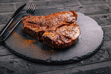 T-bone grilled beef steak with spices on black serving plate