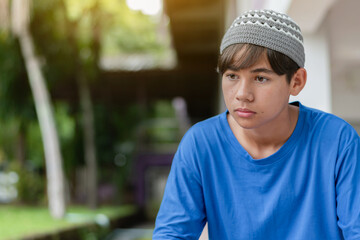 Portrait of a thoughtful teenage boy wearing a crochet cap and blue shirt, sitting outdoors with a calm and reflective expression.