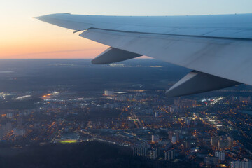 View from an airplane of the city and its surroundings. Beautiful evening aerial landscape. Buildings and streets under the wing of an airplane. Flying on an airplane. Travel and aviation tourism.