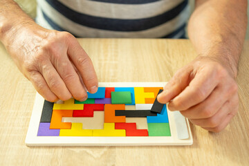 senior man's engaged hands skillfully maneuver colorful wooden pieces brain teaser puzzle,...