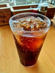 Iced Dark Soda in Clear Plastic Cup on Wooden Table