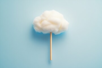 Fluffy white cotton cloud shape atop a wooden stick against a light blue background