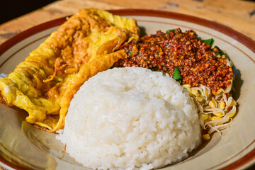 Nasi pecel or sega pecel is a typical Javanese Indonesian rice dish served with pecel. spicy hot peanuts sauce, vegetables and fried chicken egg. Wooden table. Extreme Close up view.