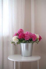 A beautiful bouquet of pink and white peonies in a silver bucket brightens a room with elegance and cheer