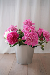 A beautiful arrangement of Pink Peonies displayed in a Silver Bucket on a Wooden Floor