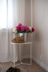 A beautiful bouquet of pink and white peonies in a silver bucket on white round table brightens a room with elegance and cheer