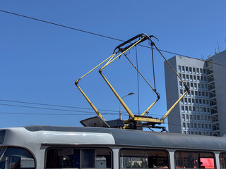 Tram pantograph and overhead lines against a clear blue sky with a modern building, concept of...