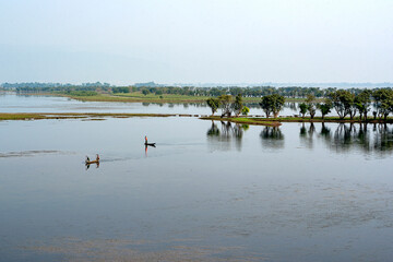 Fishermen Rowing Wooden Boats on Calm River Amidst Green Trees