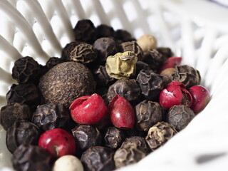 Close-up: Vibrant mixed peppercorns fill a textured white bowl.