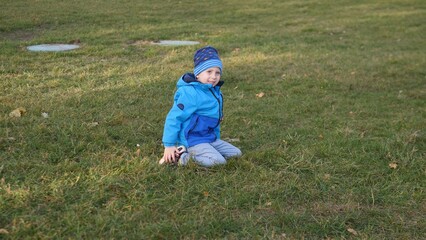Brightly dressed child sits on the grassy ground in the park, smiling and enjoying a carefree moment under the clear autumn sky, surrounded by nature's calmness.