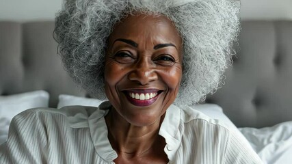 Senior woman with beautiful afro hair smiles happily while sitting in bed during morning light, Cheerful senior woman with beautiful afro hair Smiling sitting on the bed Cinematic - Powered by Adobe