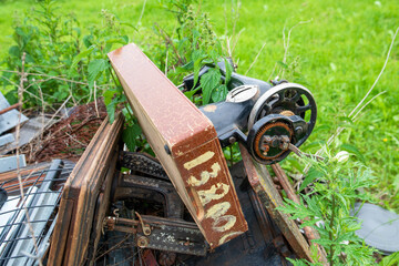 Abandoned Vintage Sewing Machine Overgrown with Weeds and Rusting Outdoors in Rural Green Grass
