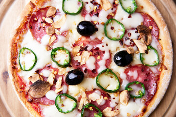 Pizza with salami and mozzarella cheese, jalapeno pepper and black olives. Wooden background. Soft focus. Close up.	