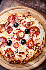Pizza with salami and mozzarella cheese, jalapeno pepper and black olives. Wooden background. Soft focus. Close up.	