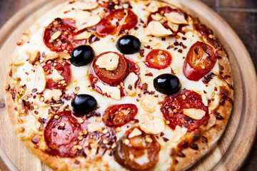 Pizza with salami and mozzarella cheese, jalapeno pepper and black olives. Wooden background. Soft focus. Close up.	