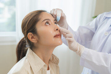 Health care concept, eye doctor eye drops to asian young woman patient, hand using medical eye drop...