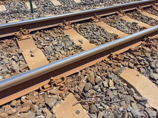 Close up of train tracks with metal rails, wooden sleepers, and gravel ballast under sunny...