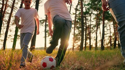 Family team, sports games. Children sons play football with father on lawn. Boys kids parent run after red ball in park. Active happy family, child dad having fun playing ball on green grass. forest