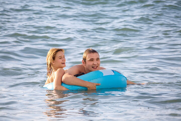 A cheerful young couple swims in the sea with an inflatable circle