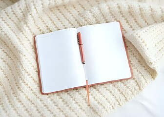  cozy cream knit blanket is spread on a bed, with a notebook and a rose gold pen placed on top, creating a calm and elegant workspace or relaxation setting.