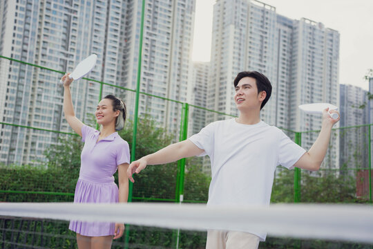Young adults playing pickleball in an urban park surrounded by high-rise buildings during late afternoon