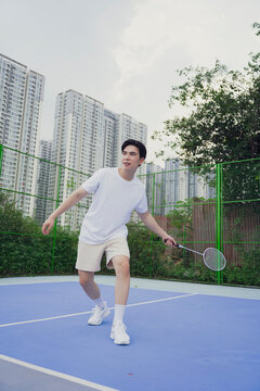 Young man plays badminton on a sunny day at an outdoor court surrounded by tall buildings in an urban setting