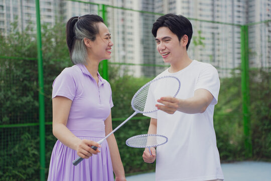 Young adults enjoy a friendly badminton match on a sunny day in an urban park with green surroundings