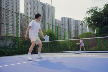 Obraz premium Pickleball match between two players on an urban court surrounded by high-rise buildings during a sunny day