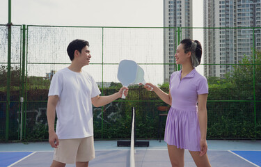Two players engage in a friendly pickleball match on an outdoor court surrounded by high-rise...