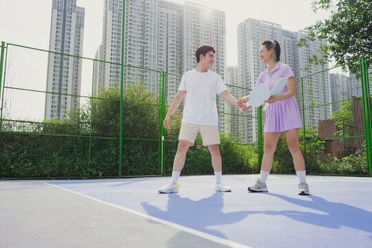 Two young adults enjoying a friendly pickleball match on an outdoor court in an urban setting during a sunny day