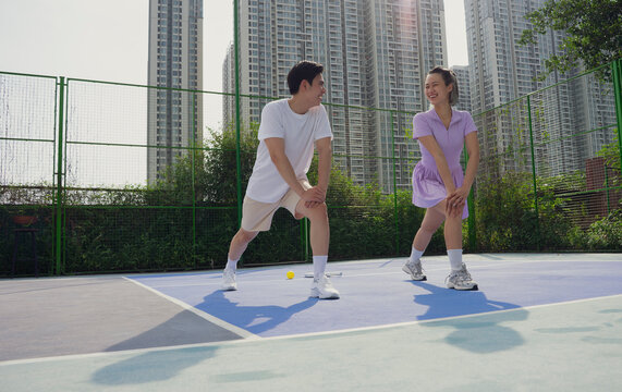 Young Asian adults engage in warm-up exercises on a pickleball court in an urban setting before their game