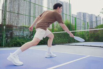 Pickleball match at an urban court featuring a young Asian male player in action during the...