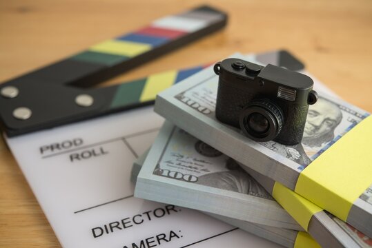 Digital camera on stack US dollar bill banknotes and clapperboard. Sell content photo or video clips and making money in stock photo microstock online website or mobile app, passive income concept.