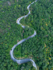 High-angle view of the road cuts through the forest on both sides. vertical Winding mountain road. A green forest from a high angle with a drone.