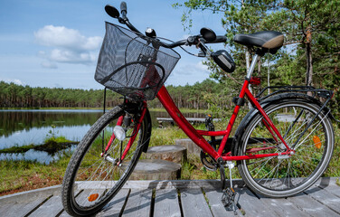Red City Bicycle with Basket Parked on Wooden Boardwalk by Forest Lake on a Sunny Day in Summer Nature Landscape