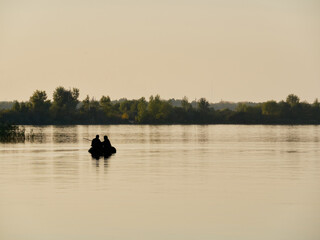 Obraz premium Two people in a small boat on a calm lake or river at sunset, silhouetted against the serene sky.