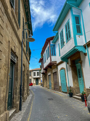 Narrow cobblestone street lined with historic buildings featuring colorful shutters and balconies under a bright blue sky in a Mediterranean old town.