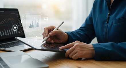 Businessperson analyzing financial data on a tablet, laptop and digital pen, modern office environment.