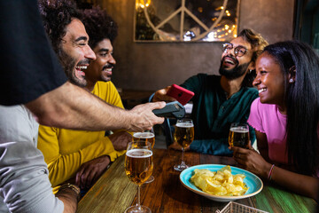 Cheerful friends paying with smartphone nfc technology in a bar at night