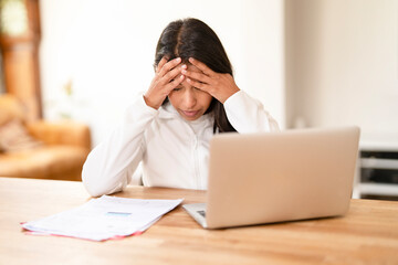 Stressed woman working at home feeling overwhelmed by tasks while sitting at her desk with a laptop...